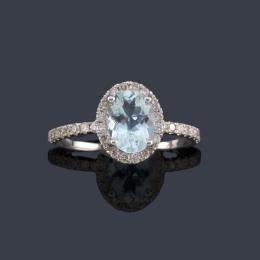 Lote 2480: Anillo con aguamarina talla oval con brazos y orla de brillantes en montura de oro blanco de 18K.