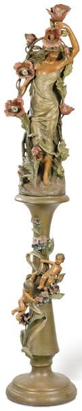 Lote 1100: Lámpara de pie modernista en terracota policromada pp. S. XX.<br>Formada por escultura de mujer con luces y peana con niños y vegetación.