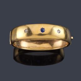 Lote 2025: Brazalete rígido con dos diamantes talla antigua y zafiro en montura de oro amarillo de 18K. Ppios S. XX.