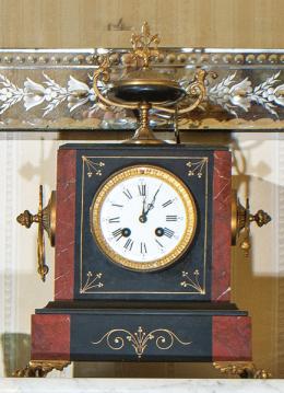 Lote 82: Reloj de chimenea con guarnición de candelabros Napoleón III en mármol negro y rojo con montura de latón. Maquinaria tipo París con sonerías de horas y medias. (Falta campana). Francia, finales del siglo XIX.