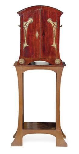 Lote 1327<br>Mueble bar modernista en madera de caoba con aplicaciones de bronce. Sobre mesa con patas recortadas unidas por balda inferior.<br>Principios S. XX