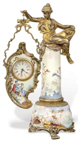 Lote 1050: Reloj de mesa de plata sobredorada y esmalte, Viena h. 1900.<br>En forma de columna rematada por una mujer sentada en bulto redondo, que sostiene la esfera.