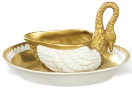 Lote 1263: Taza salsera Carl Thieme de Postchappel Dresden en forma de cisne. Esmaltada en blanco y parcialmente dorada. Acompañada de un plato oval a juego esmaltado y dorado. Ambas piezas cuentan con firma en la base. Alemania, principios del siglo XX.